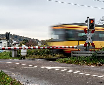 Bahnübergang in dörflicher Umgebung mit vorbeifahrender Bahn
