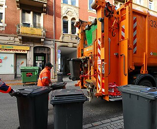 Zwei Müllmänner schieben Mülltonnen zum Abfallsammelfahrzeug.