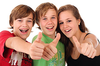 Drei Jugendliche, die in die Kamera lächeln und Daumen nach oben zeigen.