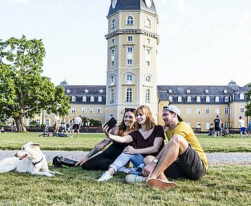 Das Bild zeigt Studierende mit einem Hund im Schlossgarten.
