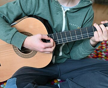 Kind spielt Gitarre sitzend auf dem Boden.