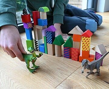 Ein Kind spielt mit zwei Dinosauriern vor aufgetürmten Bauklötzen.