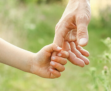 Nahaufnahme einer Kinderhand, die sich an einer Erwachsenenhand festhält.