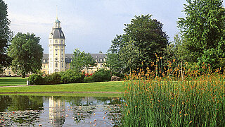 Das Bild zeigt einen Teil des Schlossgartens mit Teich und Schlossturm.