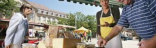 Das Bild zeigt einen Marktstand mit Käse auf dem Stephanplatz