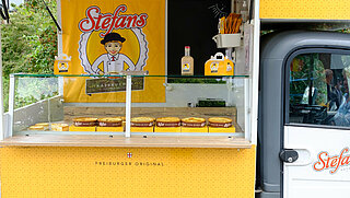 Das Bild zeigt ein kleines gelbes Verkaufsmobil mit Käsekuchen.