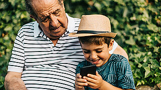 Ein Opa schaut mit seinem Enkel zusammen auf ein Smartphone