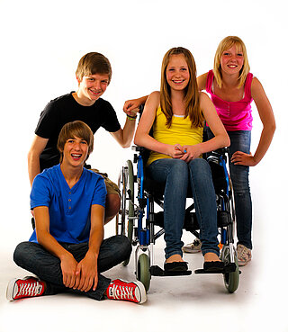 Vier Jugendliche: ein Mädchen sitzend im Rollstuhl, zwei  Jugendiche stehend, einer im Schneidersitz sitzend