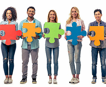 Fünf junge Menschen die große Puzzleteile in den Händen halten
