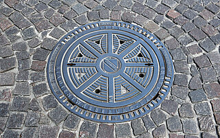 Das Foto zeigt einen städtischen Schachtdeckel mit dem Logo der Stadt Karlsruhe.