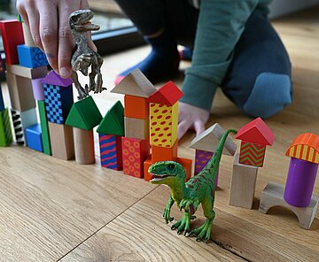 Bild spielt mit Dinosaurier und Bauklötzen.