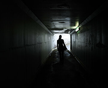 Schatten einer jungen Frau, die allein durch einen dunklen Tunnel läuft.