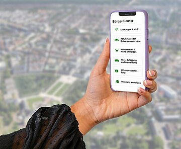 Das Bild zeigt ein Smartphone-Display mit einer Auswahl an eServices, im Hintergrund eine Panoramaansicht von Karlsruhe.