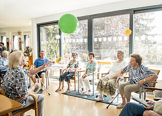 Seniorinnen und Senioren sitzen im Kreis und werfen sich einen Luftballon zu.