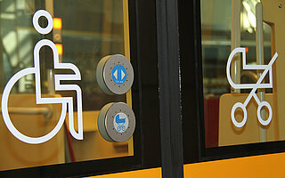 Die Abbildung zeigt eine Straßenbahntür mit Symbolbildern für Rollstuhlfahrende und Familien