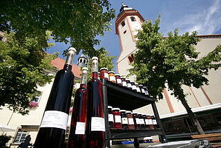 Das Bild zeigt rote Likörflaschen. Im Hintergrund ist das Rathaus Durlach zu sehen.