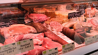 Das Bild zeigt einen Marktstand mit Fleischwaren auf dem Stephanplatz
