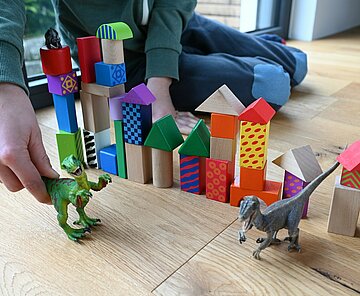 Ein Kind spielt mit zwei Dinosauriern vor aufgetürmten Bauklötzen.