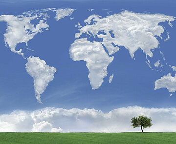 Das Symbolbild zeigt eine Weltkarte aus Wolken über grüner Wiese.