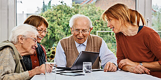 Ältere Menschen sitzen gemeinsam am Tisch und schauen auf den Bildschirm eines Laptops.