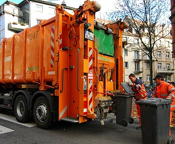 Müllwagen mit Abfalltonnen, die von zwei Mitarbeitern geleert werden