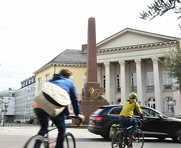 Radfahrende vor der Verfassungssäule am Rondellplatz.