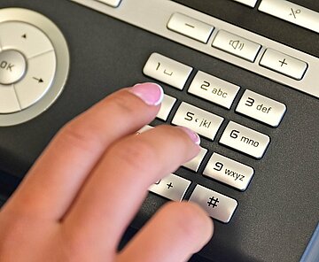 Das Bild zeigt ein Telefon mit der Hand einer Person, die eine Notfallnummer wählt.