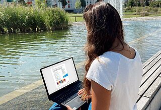 Junge Frau sitze mit Laptop auf einer Bank im Park