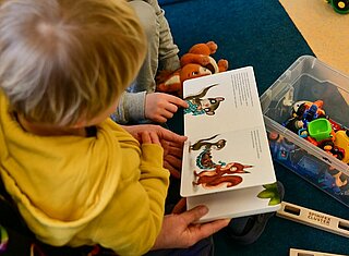 Eine Erzieherin liest mit zwei Kindern ein Buch.