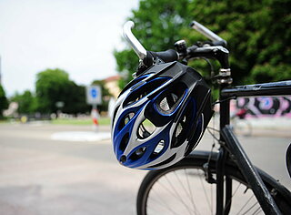 Das Bild zeigt einen Fahrradhelm, der am Lenker eines Fahrrads hängt.