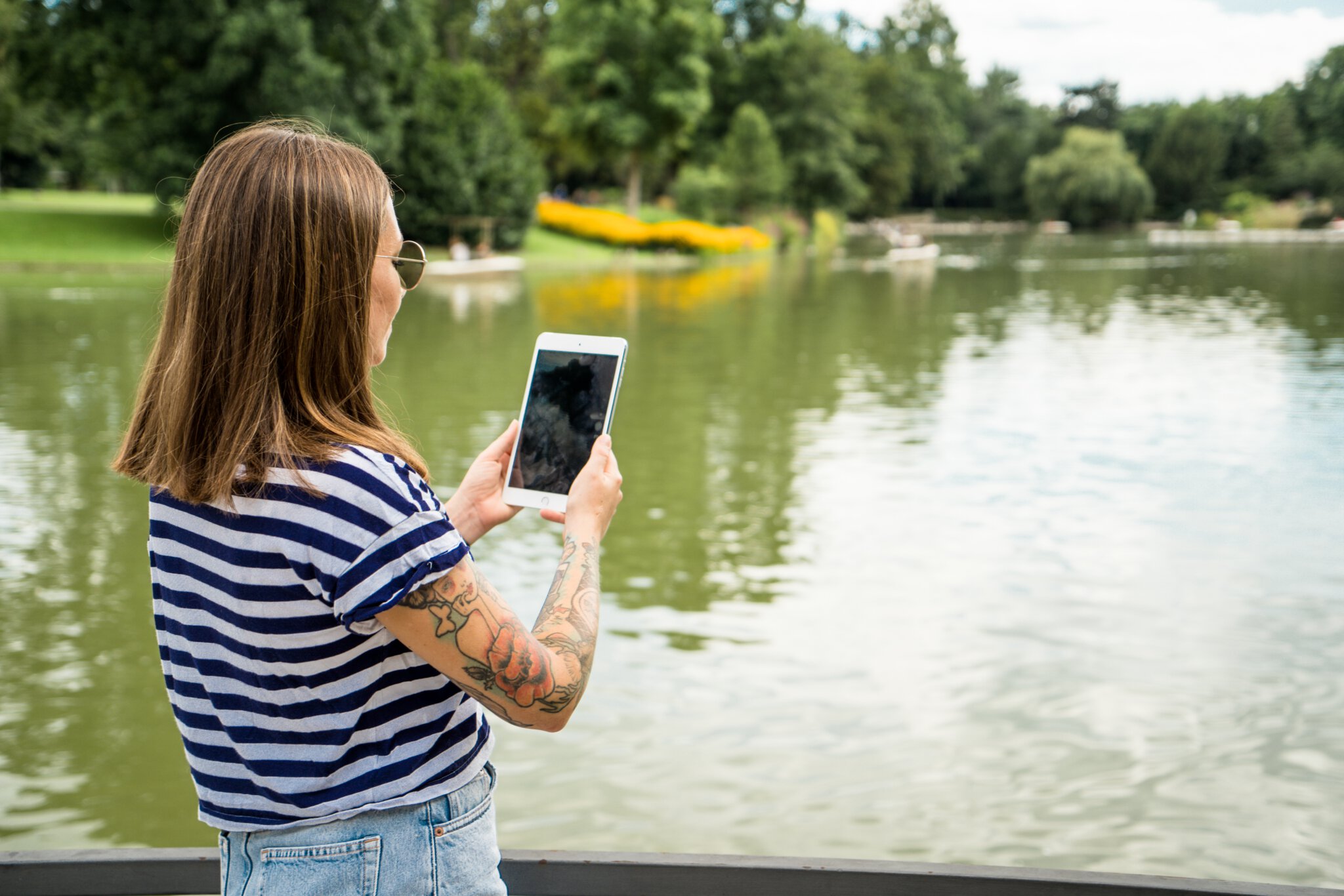 Eine junge Frau fotografiert den vor ihr liegenden See mit ihrem Tablet.