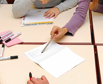 Person zeigt am Tisch mit Schreibgerät auf ein Schriftstück.