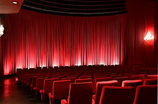 Sitzreihen im Kinosaal mit geschlossenem Vorhang vor der Leinwand.