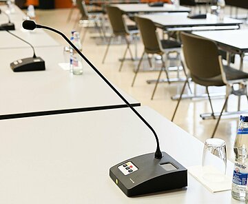 Einzelne Tische mit Mikrofonen im großen Sitzungssaal