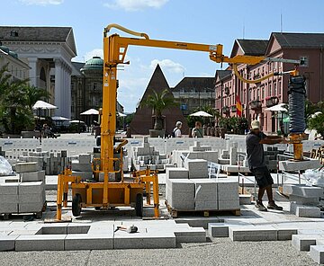 Mit einem Spezialgerät verlegen Bauarbeiter das Granitpflaster am Marktplatz.