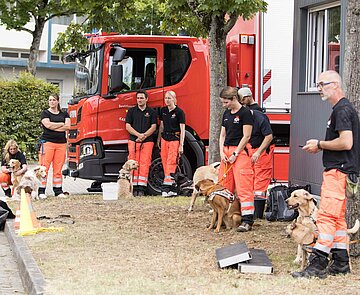 Feuerwehrmänner und -frauen stehen vereinzelt mit Hunden zusammen