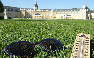 Symbolbild: Thermometer mit Sonnenbrille auf der Wiese vor dem Karlsruher Schloss