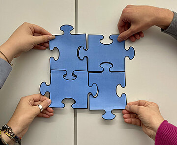 Vier Puzzleteile werden von Händen zusammengefügt. 