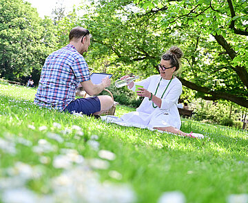 Zwei Personen sitzen auf einer Wiese im Park.