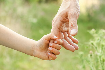 Nahaufnahme einer Kinderhand, die sich an einer Erwachsenenhand festhält.