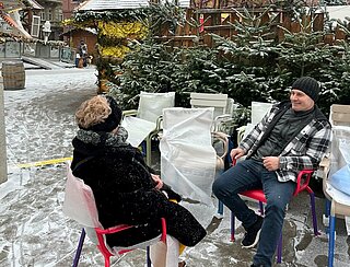 Foto von Personen in Stühlen auf dem Marktplatz mit Weihnachtsmarkt