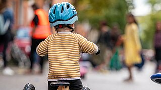 Kind mit Helm fährt auf Dreirad auf der Straße