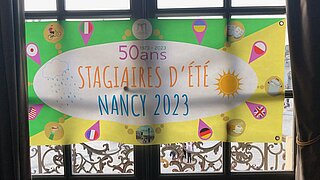 Plakat / Banner zum Jubiläum 50 Jahre Sommerpraktikum in Nancy am Fenster des Grand Salons des Rathauses Nancy