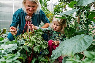 Das Bild zeigt eine Frau und ein Kind beim Gemüsepflanzen