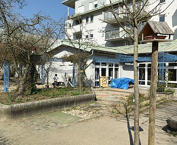 Gebäudeansicht Kindertagesstätte Blücherstraße mit Spielbereich draußen und Vogelhaus im Vordergrund