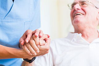 Pflegekraft hält Hand eines älterern Mannes.