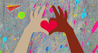 Eine dunkle und eine helle Hand formen mit den Zeigefingern und Daumen ein rotes Herz. Im Hintergrund ist eine mit bunten Farben bekleckste Betonwand.