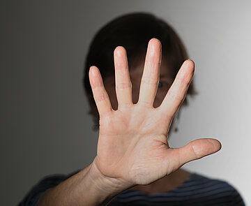 Das Bild zeigt eine Frau, die Ihre Hand hebt zur einer Geste, die Stopp! bedeutet. 