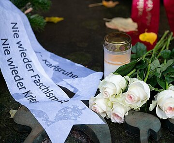 Rosen, Gedenkkerze und Kranz mit Aufschrift "Nie wieder Faschismus! Nie wieder Krieg!" am Platz der Ehemaligen Synagoge