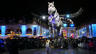 Sankt Nikolaus Umzug, hier mit einem großen beleuchteten mechanischen Pferd sowie  im Hintergrund der Triumpfbogen Arc Héré und Riesenrad